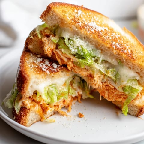 Geschmolzener Mozzarella auf einem goldenen, knusprigen Buffalo Chicken Caesar Grilled Cheese Sandwich, serviert auf rustikalem Holz.