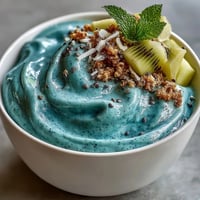 Vibrante blaue Spirulina Smoothie Bowl mit tropischen Früchten und Kokosflocken.